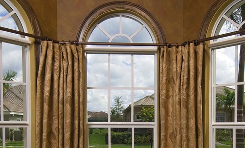 Bow windows with half-circle tops and gold draperies looking out over a Florida yard. 