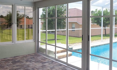 An enclosed patio with floor-to-ceiling windows and French doors opening out to a pool area.