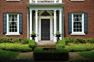 A dark front door of a Brick home with white windows and white pillars in the entryway