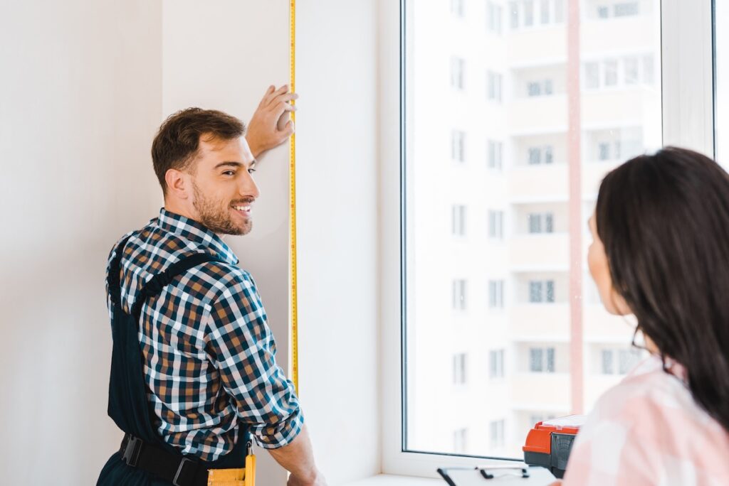Cheerful handyman measuring a window during home installation