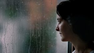 Woman standing by a window during rainy weather
