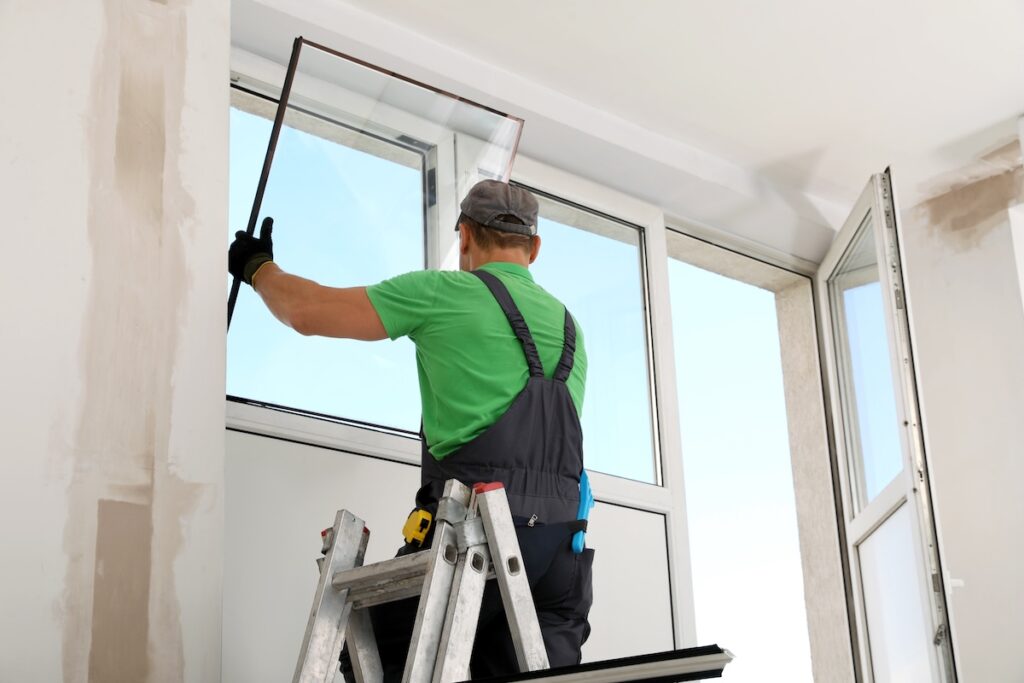 Installer fitting a new window pane into a white window frame