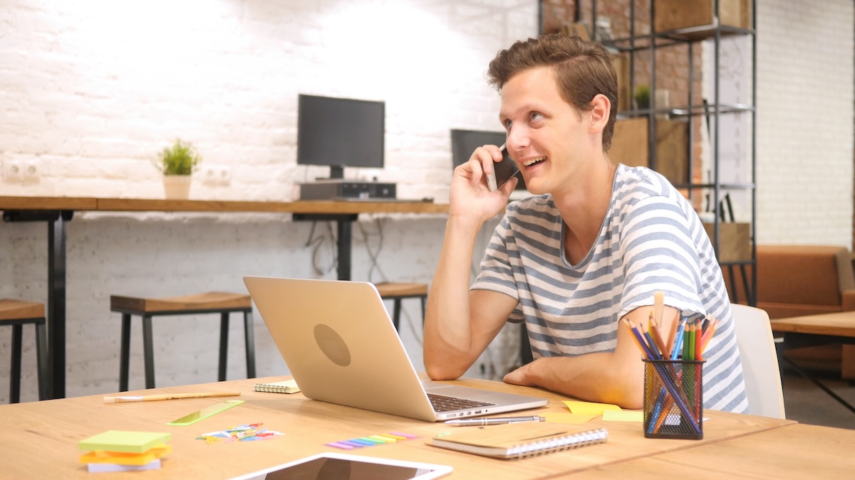 Man talking on the phone while working at a laptop in a home office