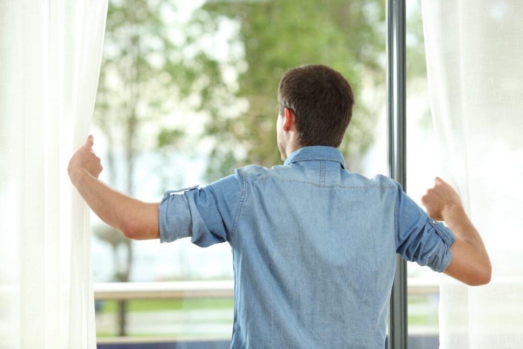 Homeowner opening curtains to check large windows before storm season