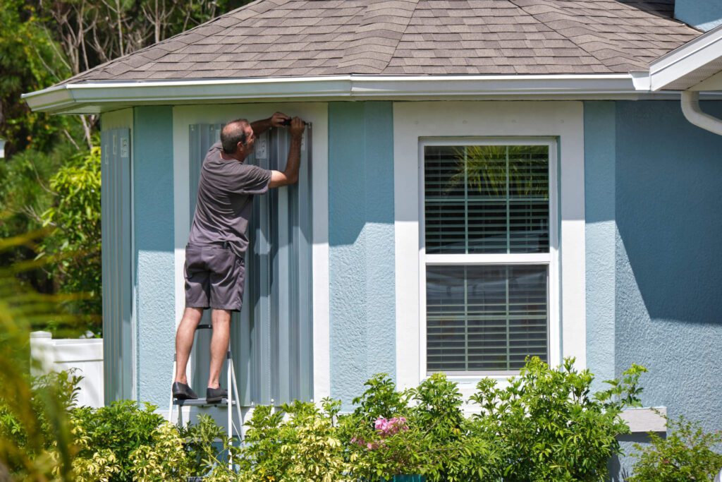 Homeowner installing steel storm panels over windows before hurricane season
