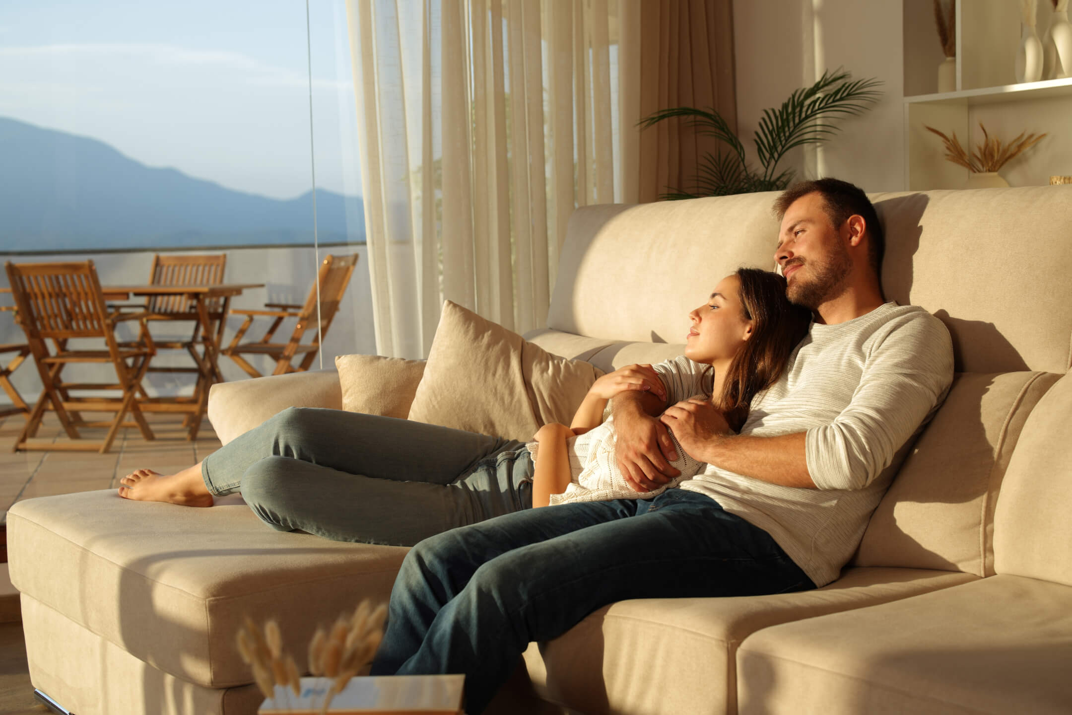 Relaxed couple sitting on a couch near bright home windows