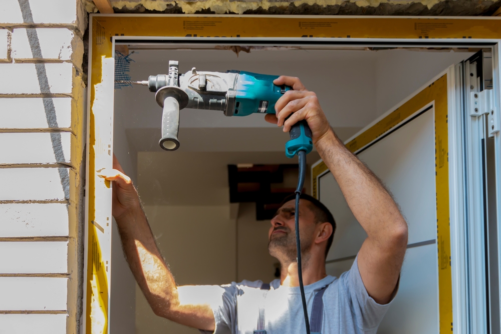 Door installer drilling into an exterior door frame during replacement installation