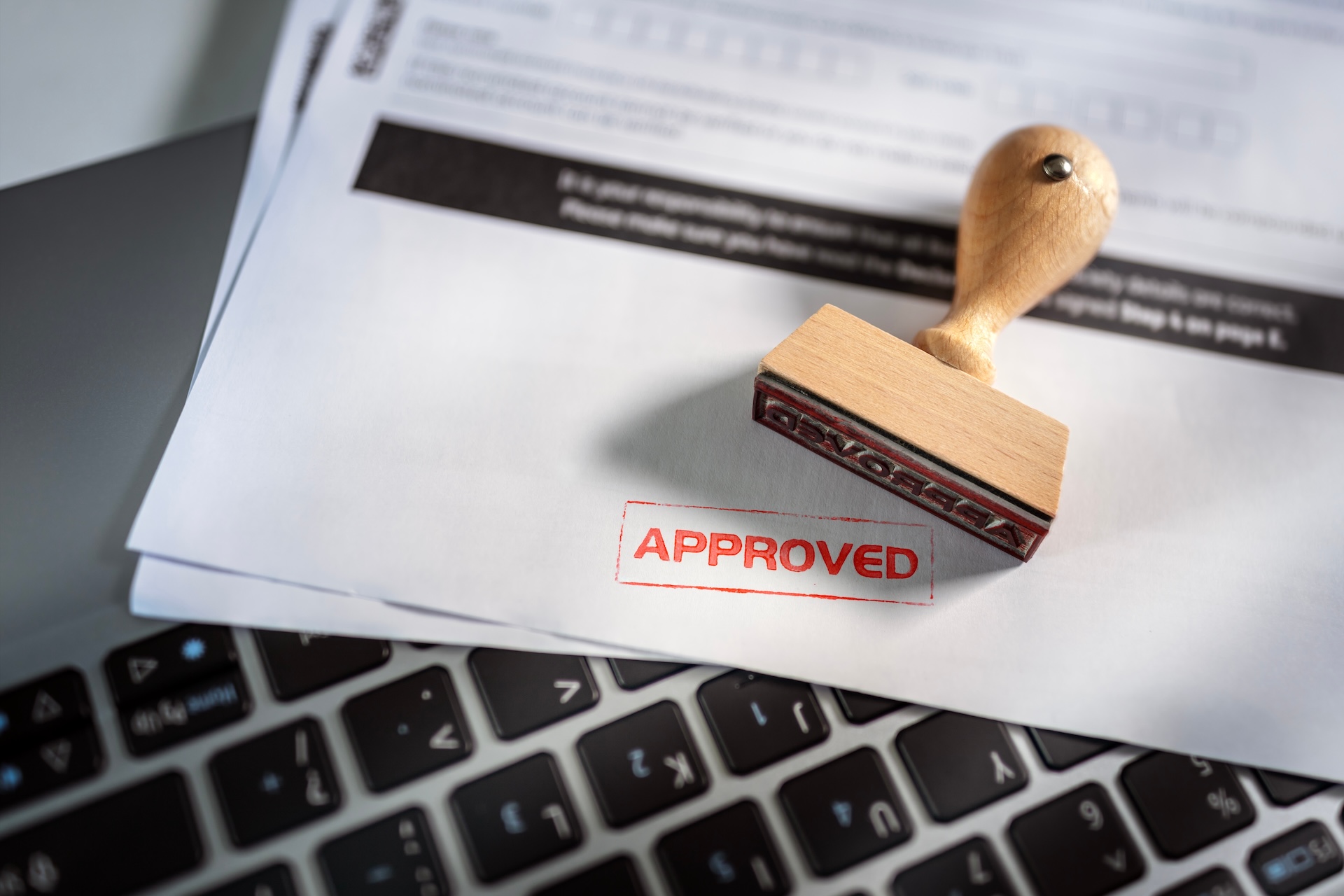 Approved document stamp on paperwork over a laptop keyboard