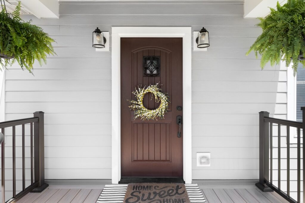 Brown front entry door on a gray house porch with black railings